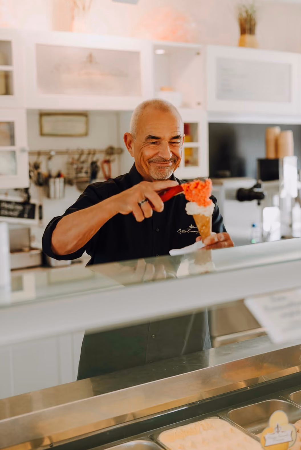 Detlef Fügeisen an der Eistheke der Sylter Eismanufaktur, während er eine Waffel mit Erdbeersorbet vollendet